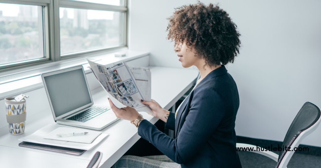 A woman sitting in front of the windows and laptop while holding a paper