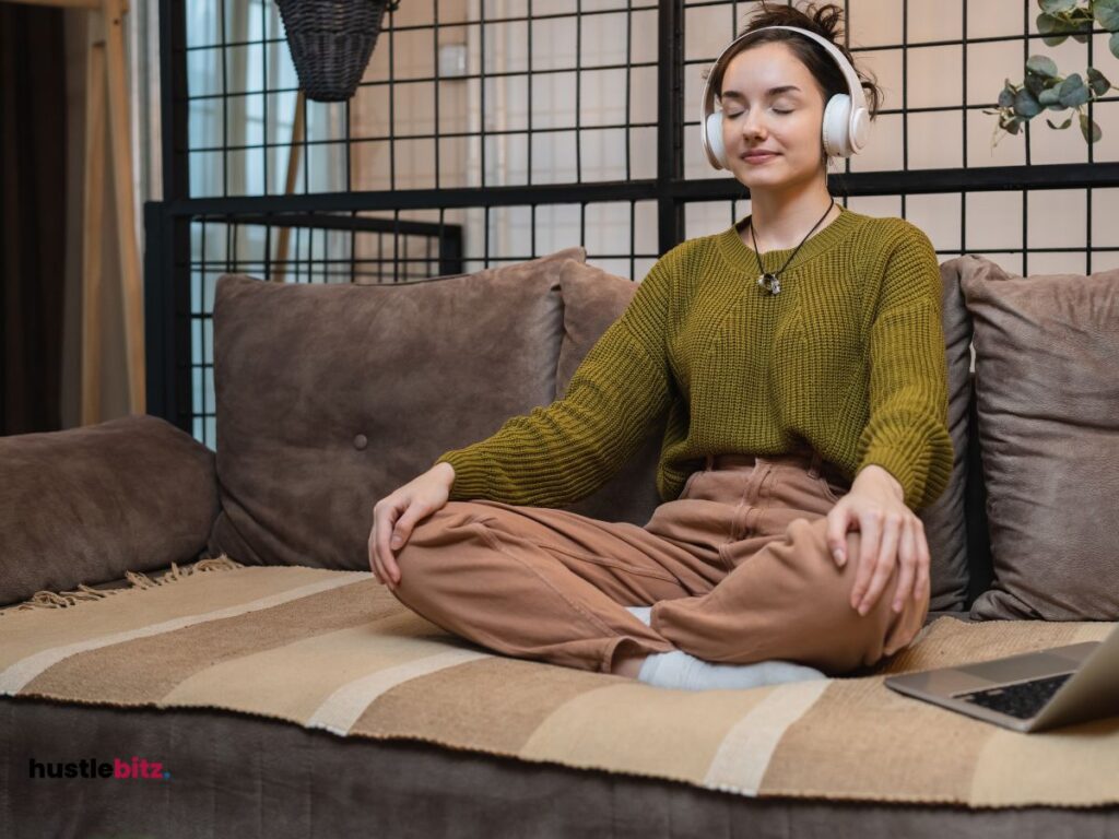 A woman sitting the couch wearing headphone while doing meditation