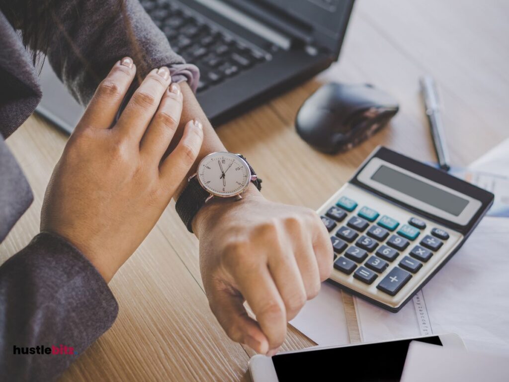 a hand wearing clock and a laptop, calculator in the table