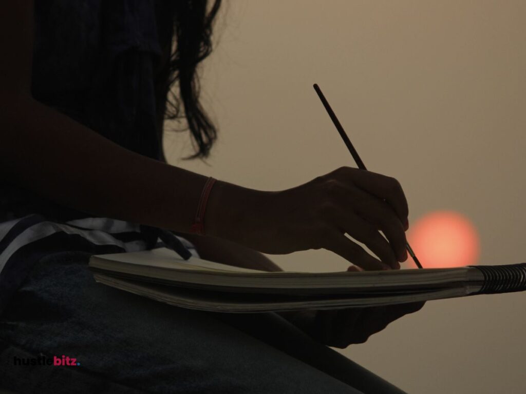 A hand of a woman holding a paint brush and drawing book