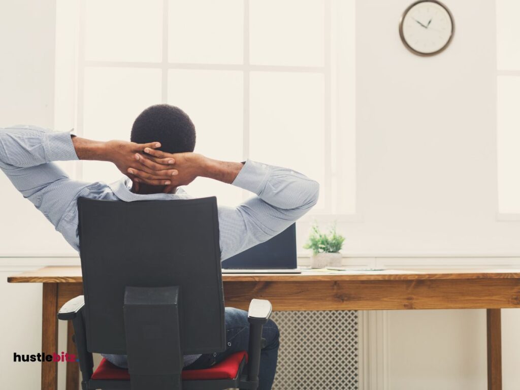 A man sit on the chair holding his head inside the office with clock on the wall