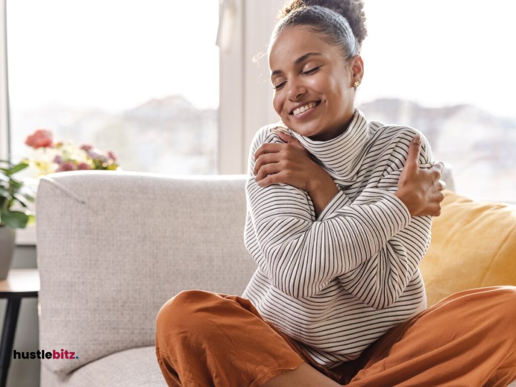 A picture of a woman hug herself and smiles while sitting in the couch