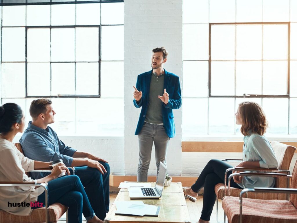 A man standing and talking to the other people sitting in the chair inside the office