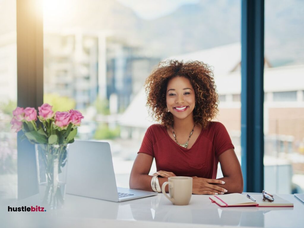 A woman sitting in the office with laptop, cup and flowers in the table