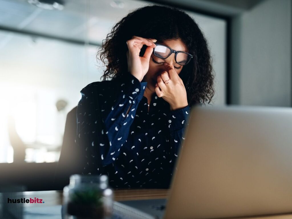 A woman holding her eyes and holding a eyeglass in front of the laptop