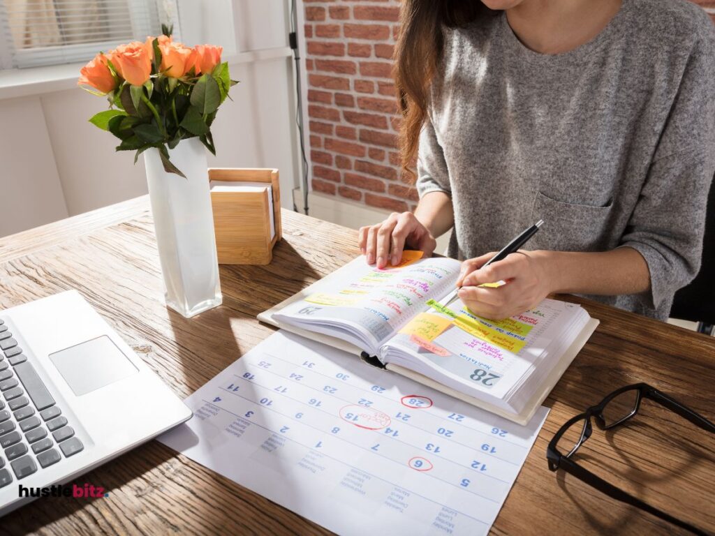 A woman doing writing in the book and a calendar with laptop in the table