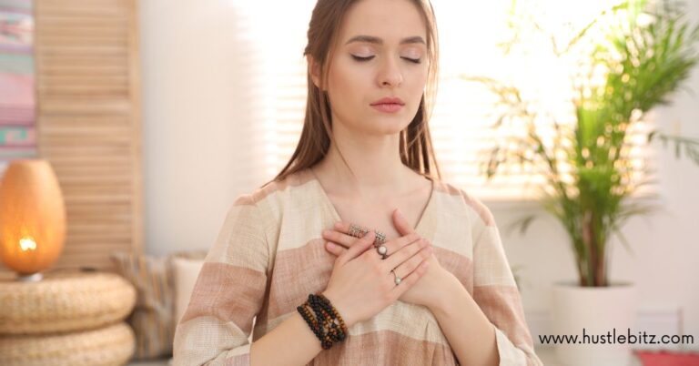 A person meditating with closed eyes, hands on their chest, in a peaceful, softly lit room.