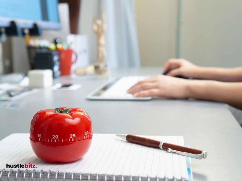 A Pomodoro, notebook, pen and a human hand in the table