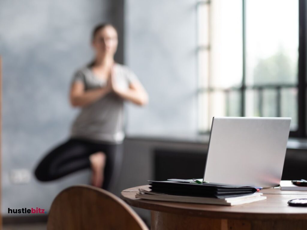 a table with laptop and a woman background doing meditation