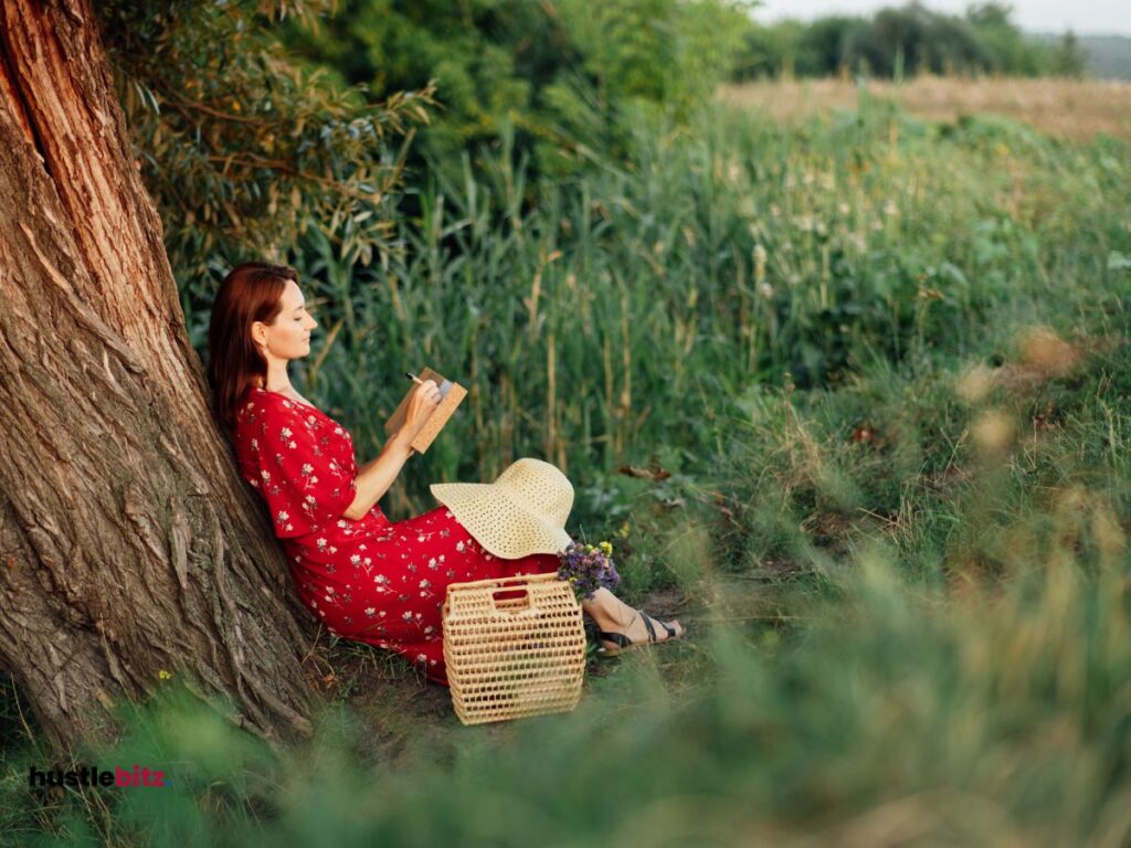 A woman sitting down the tree holding a pen and a book