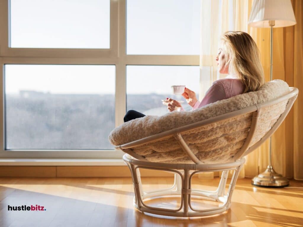 A woman holding a cup of tea sitting in the couch in front of the windows with sunlight