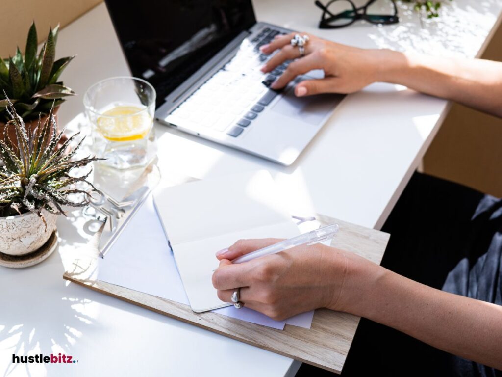 A hand doing writing and a laptop in the table