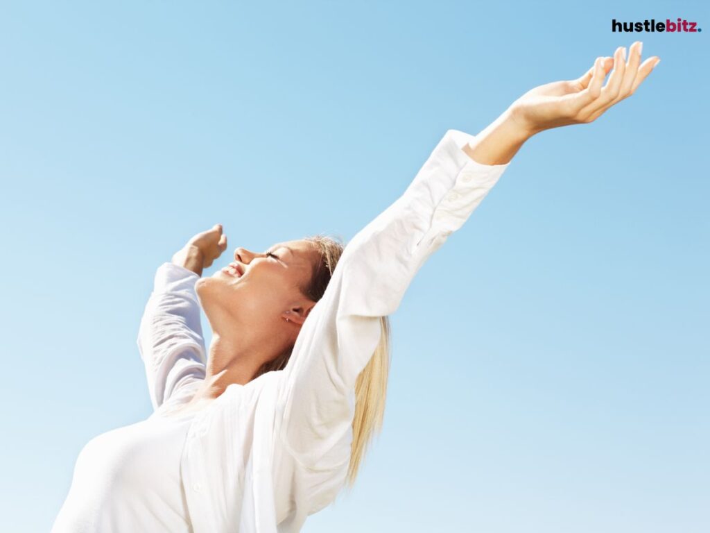 Woman smiling with arms wide open against the sky.