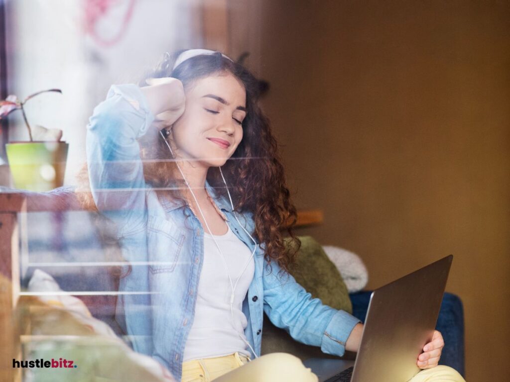 A woman wearing headphone and smiles while holding the laptop