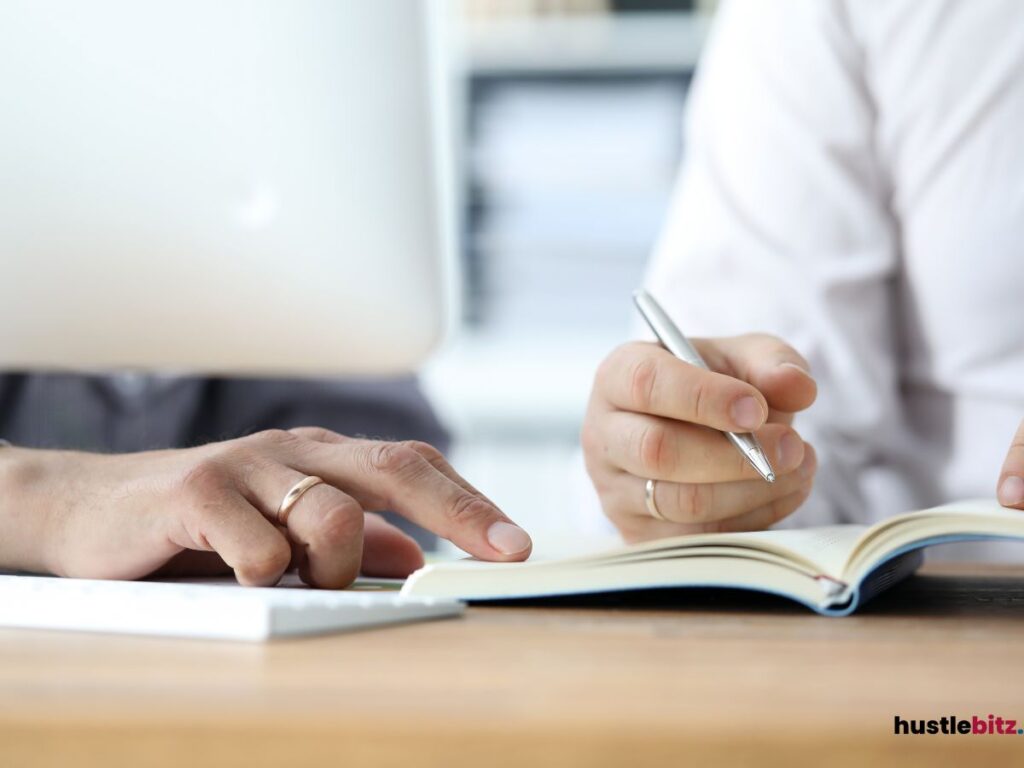 Two people collaborating, one pointing at a notebook.