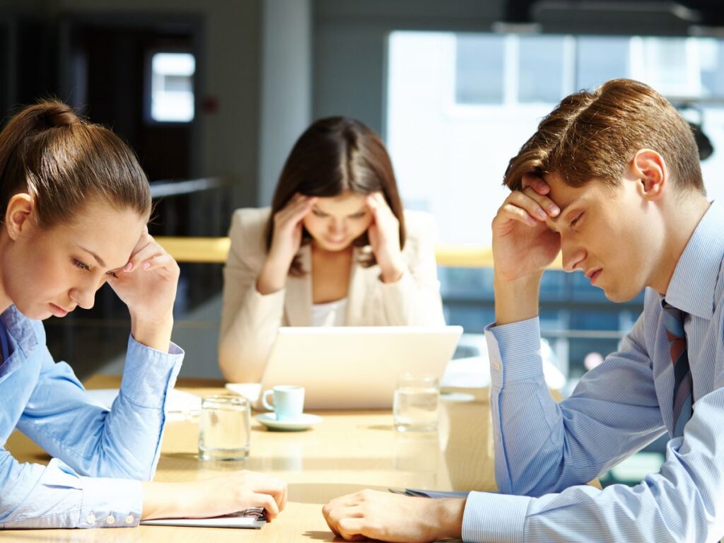 three people holding their head inside the office