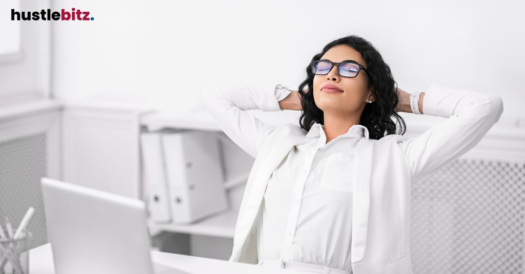 A woman in white, sitting back at her desk, feeling relaxed.