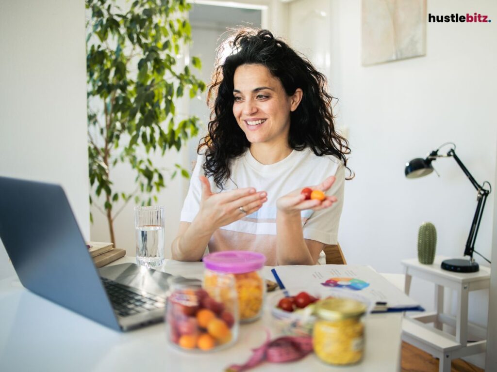Woman smiling, holding food, interacting with a laptop.