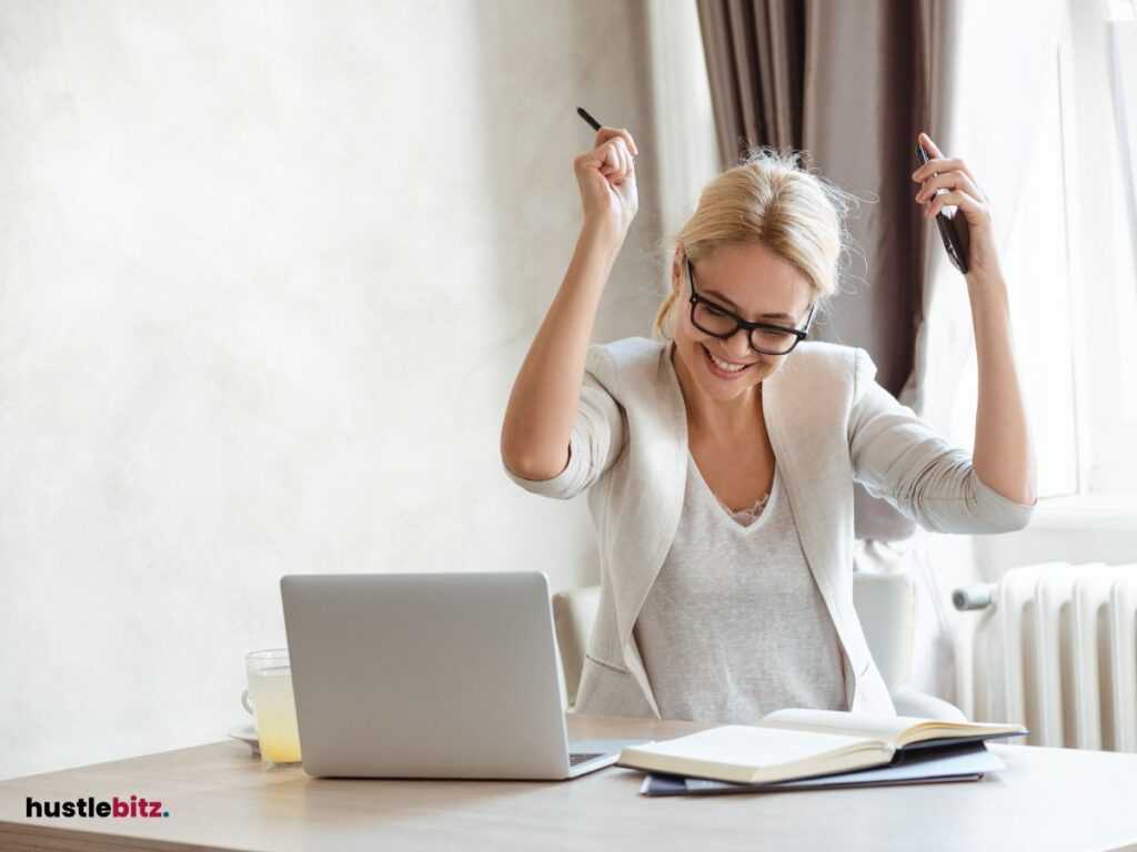 A woman raise her two hands and a laptop in the table