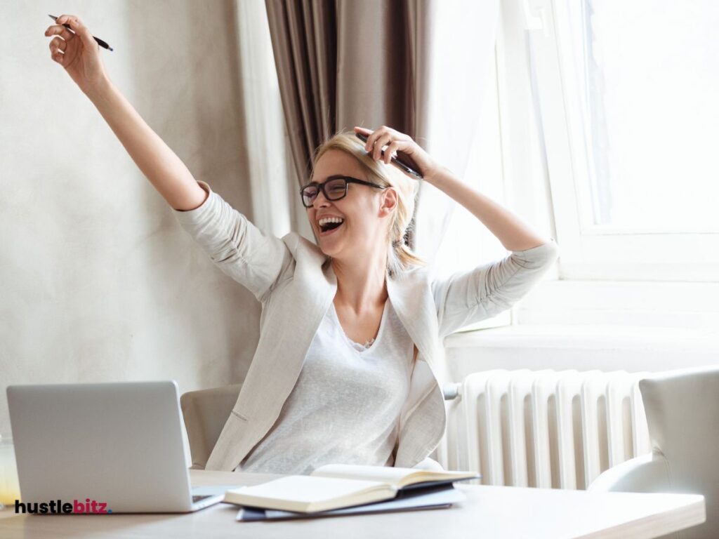A woman smiles featuring victory and a laptop in the table
