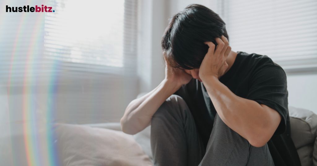 A man sitting on a couch, holding his head in his hands.