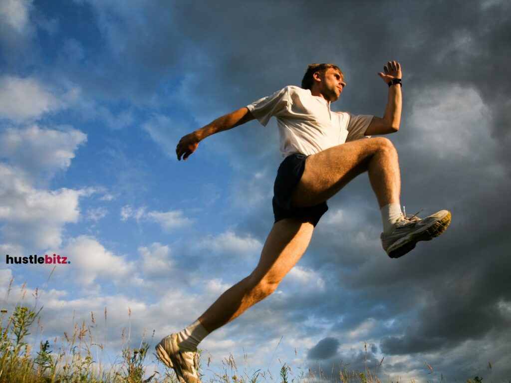 A man jumping over the field with grass.