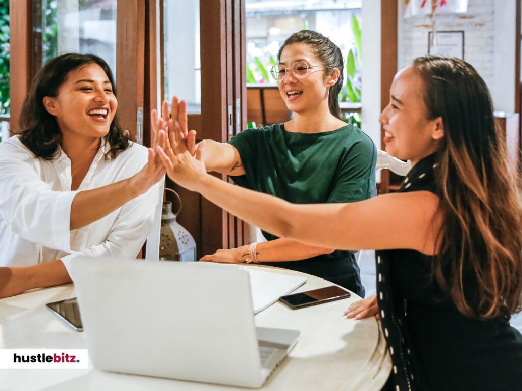 Three women hold their hands and a laptop in the table