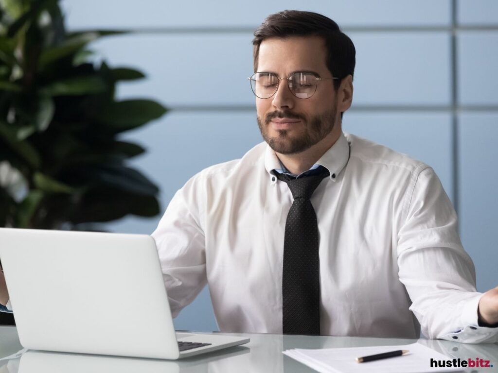 A man in business attire sitting at his desk with his eyes closed, appearing calm and meditative.