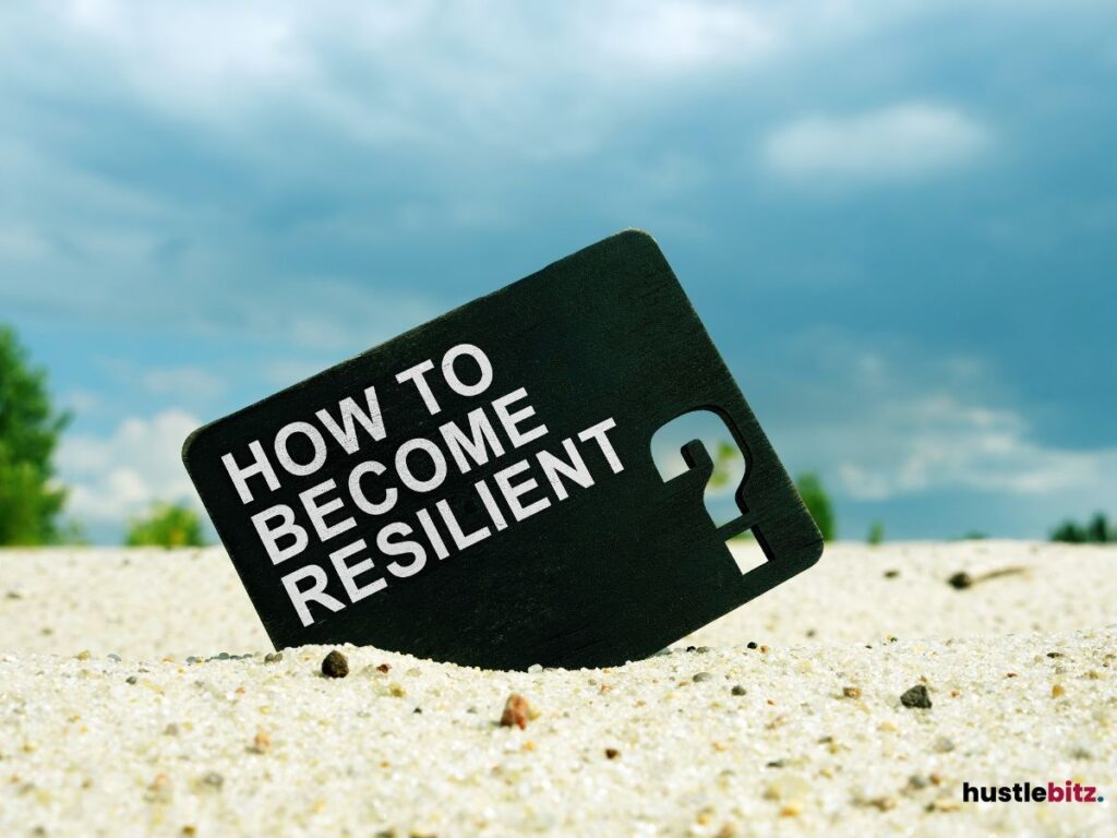 A sign in the sand asking "How to become resilient?" with a blue sky backdrop.