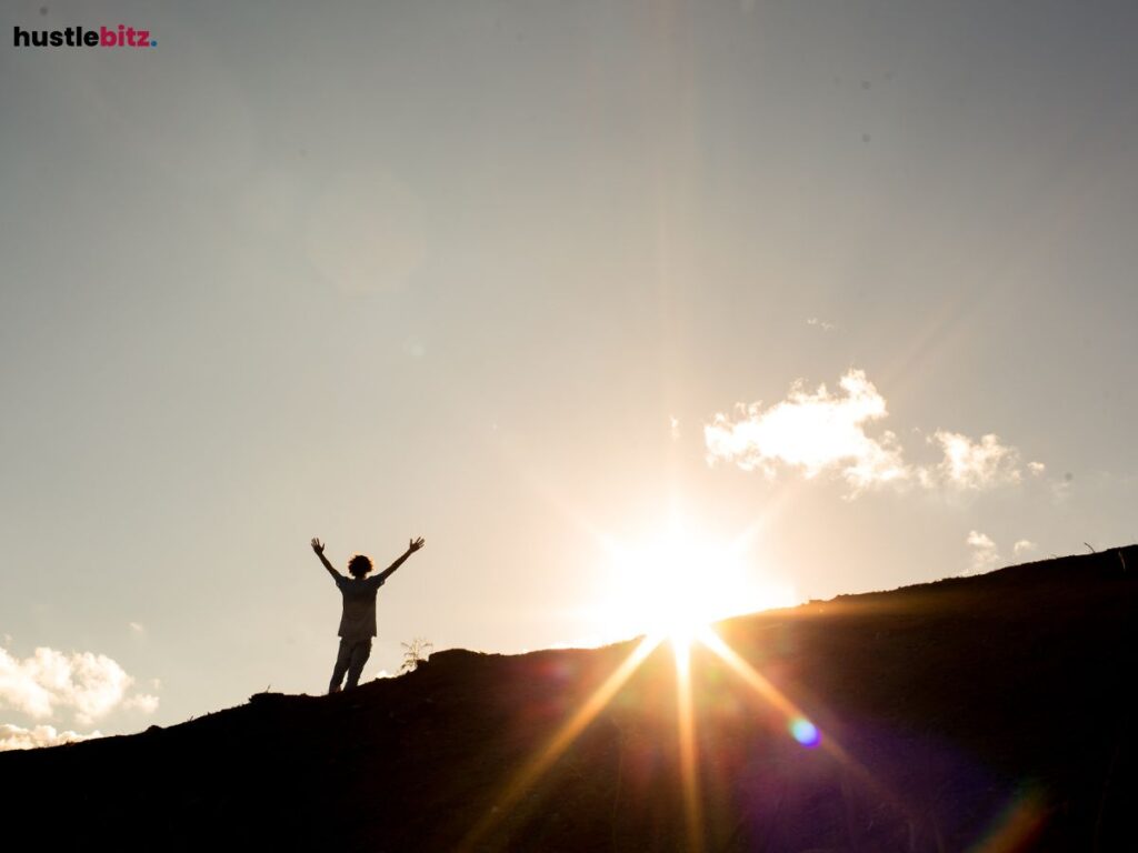A man standing on a hill with the sun shining behind him.