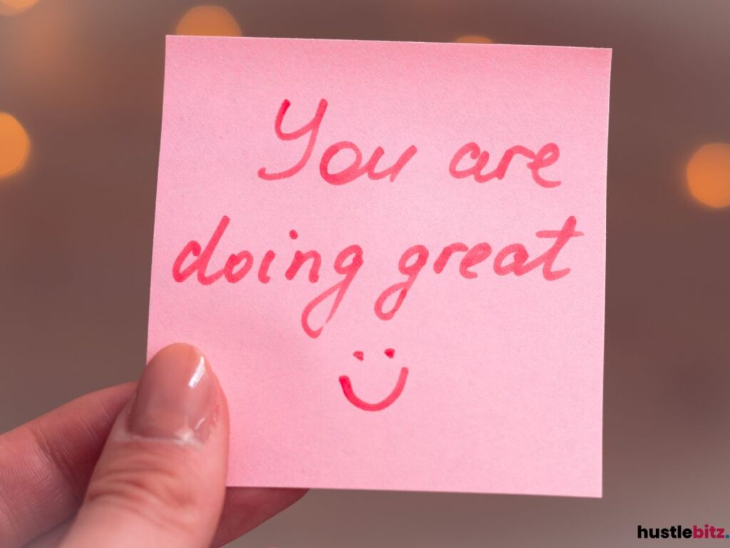 A hand holding a sticky note that says "You are doing great" with a smiley face.