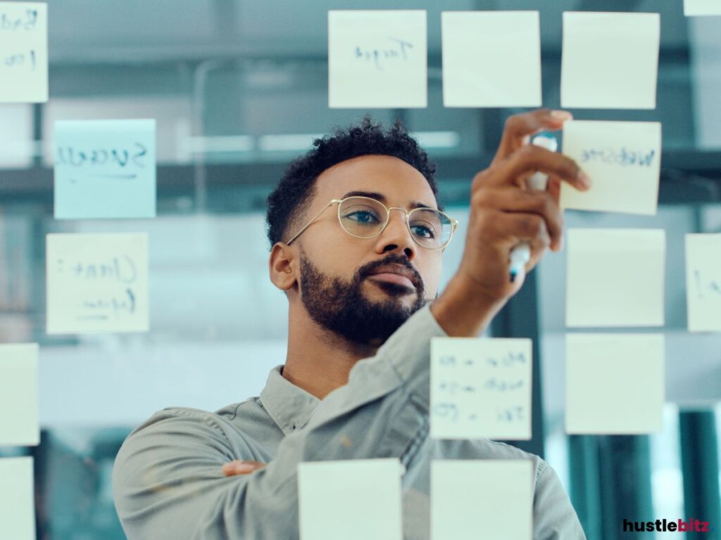 A man wearing glasses picking up the sticky note on the transparent glass.