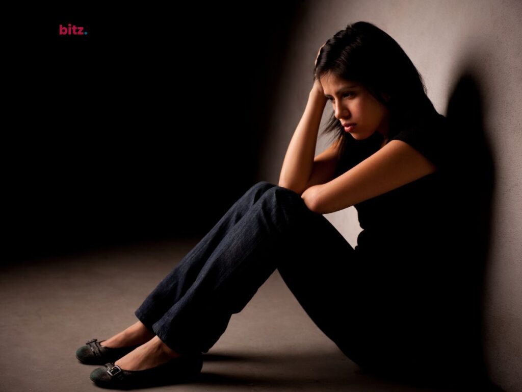  A woman sitting on the floor against a wall, looking down with her head in her hands