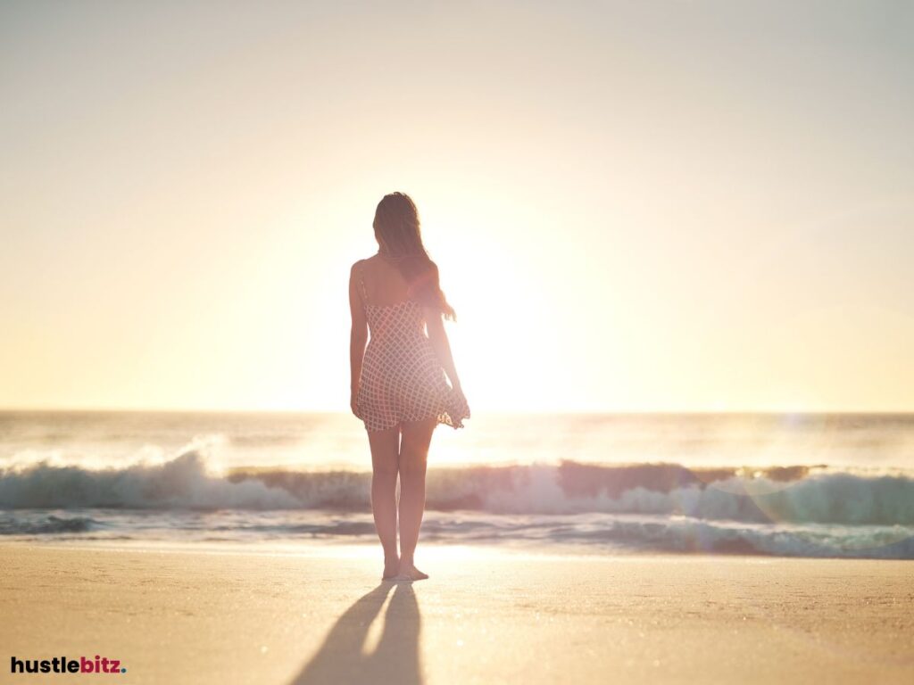 A woman facing the sea at the seashore with the sunset.