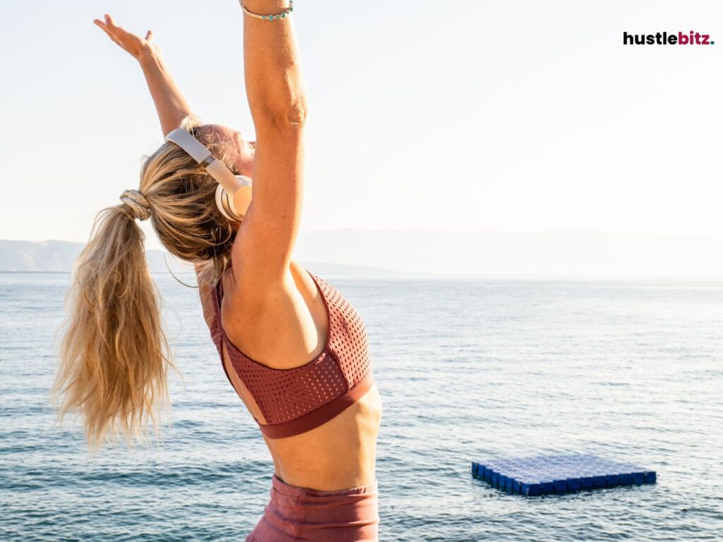A woman doing stretching beside the sea and wearing headphone