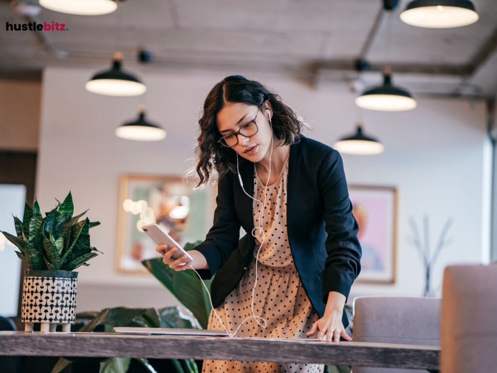 A woman wearing head set and holding her phone while looking at the desk.