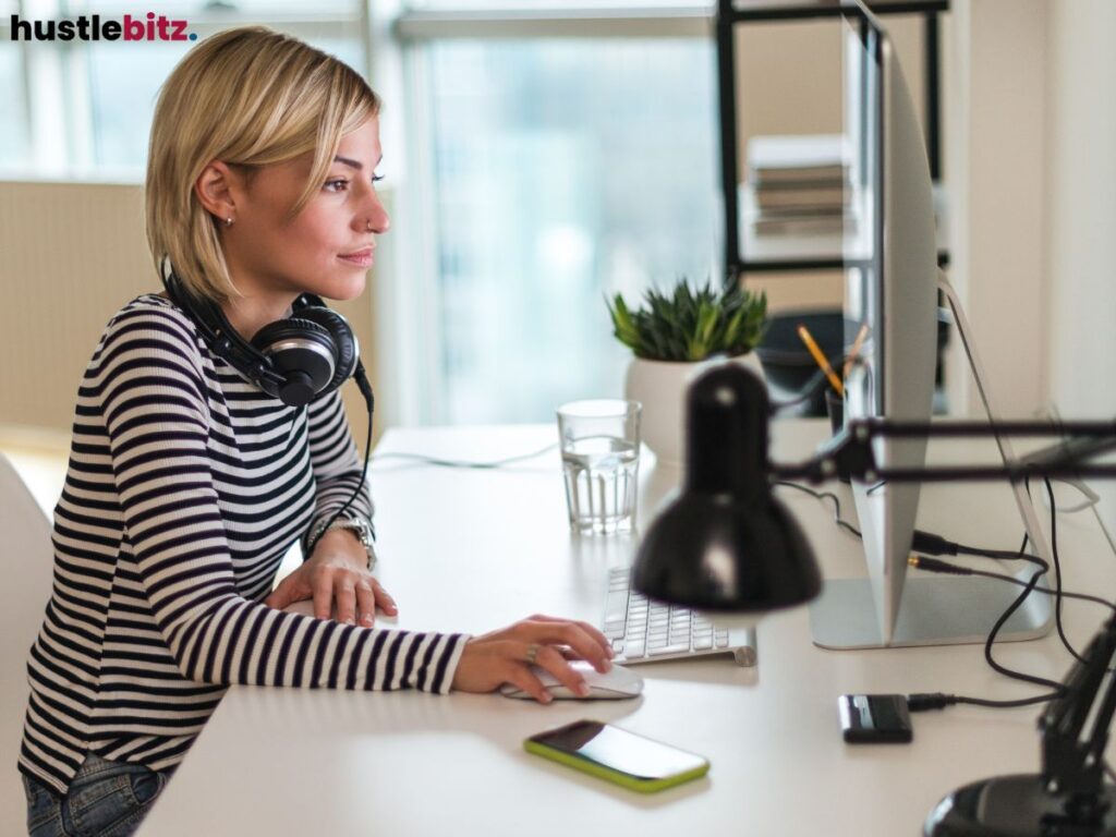 Woman working at a desk, wearing headphones, focused on a computer screen.