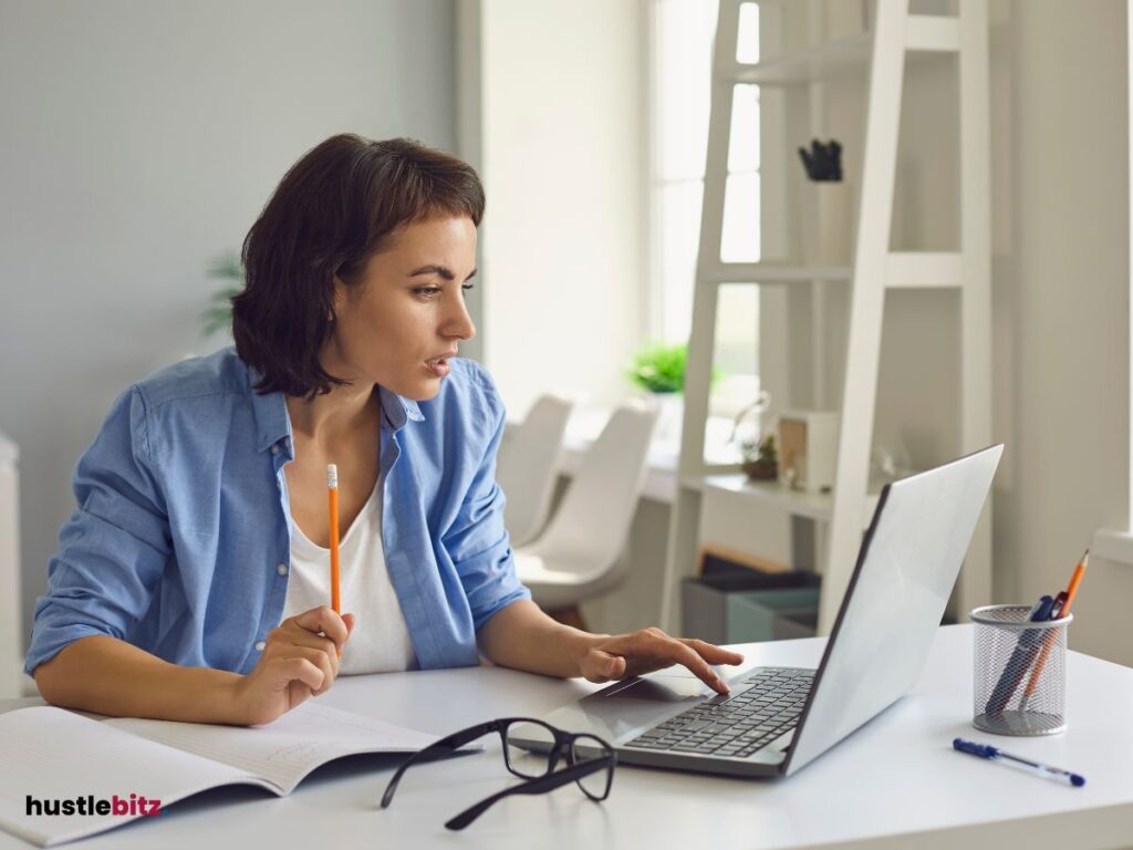 A woman looking at the laptop and holding a pencil inside the office