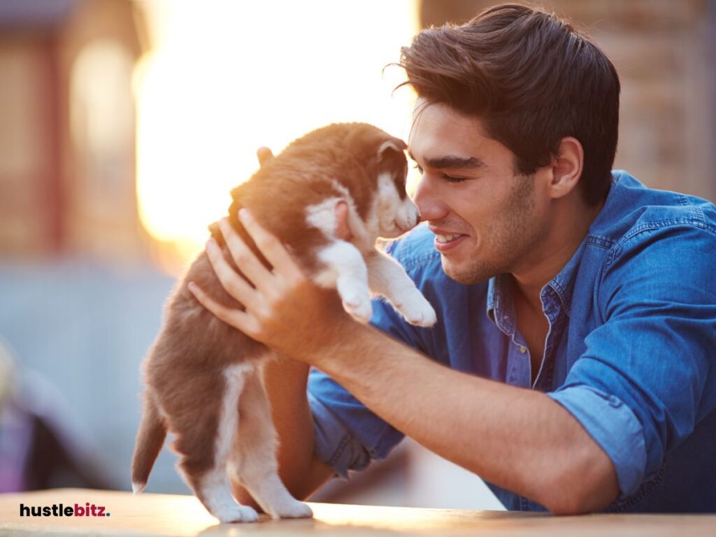 A man smiling as he lovingly holds a puppy up close.