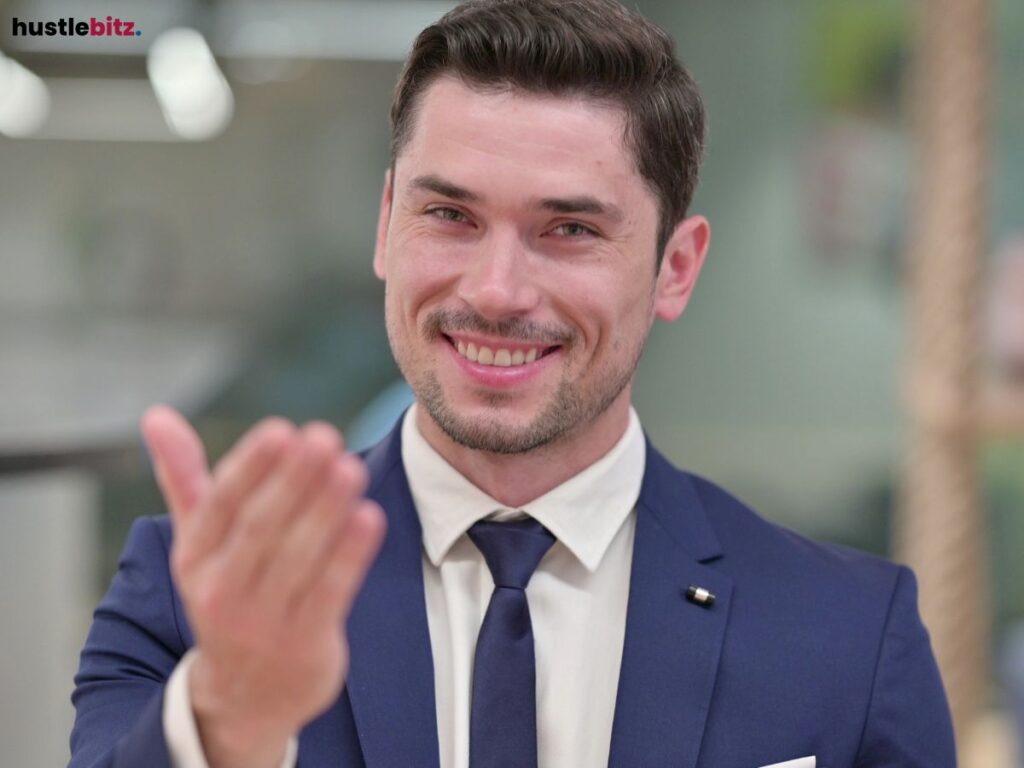 A smiling man in a suit, extending his hand as a friendly gesture.