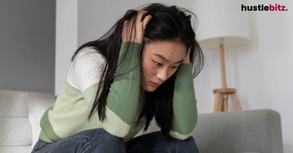 A woman holding her head in distress, sitting on a couch.
