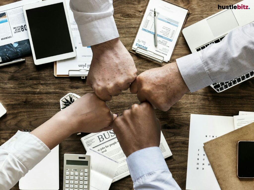 Four hands coming together for a fist bump over a desk with office items.