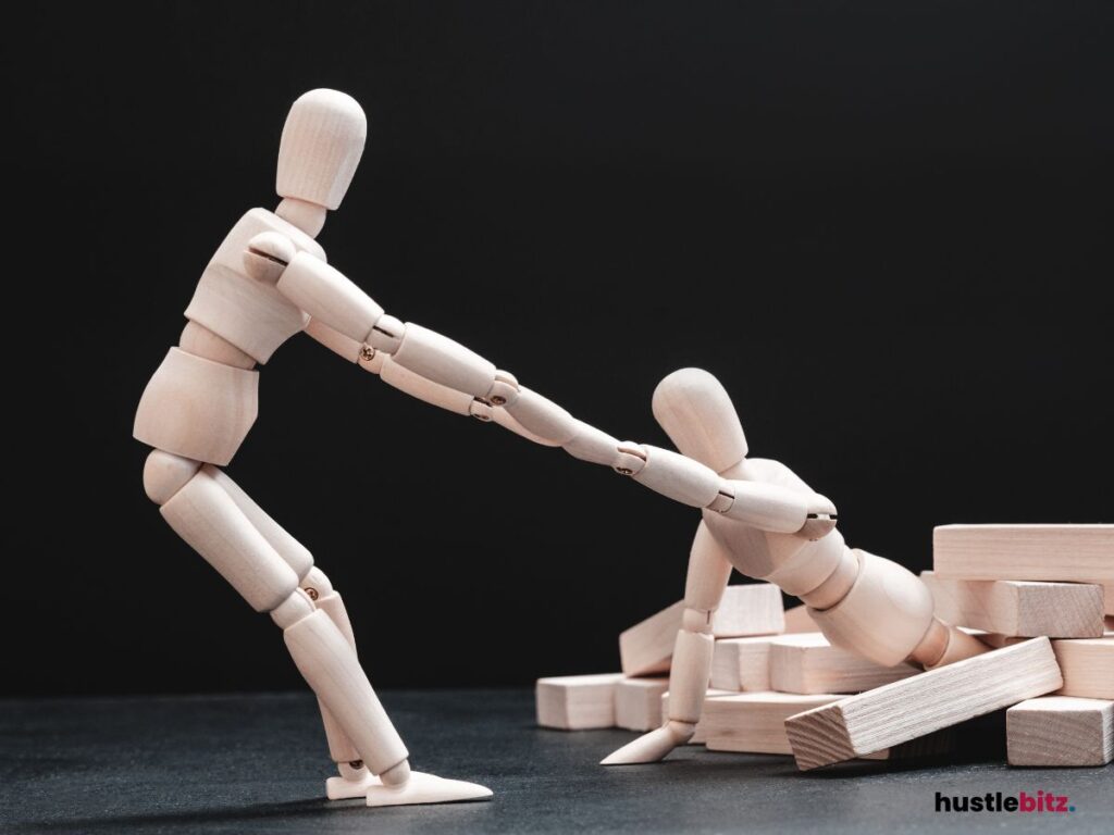 Two wooden mannequins depict one figure helping another up from a fall.