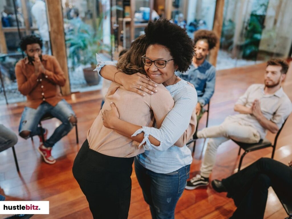 Two women hugging in a group setting, symbolizing emotional support and connection.