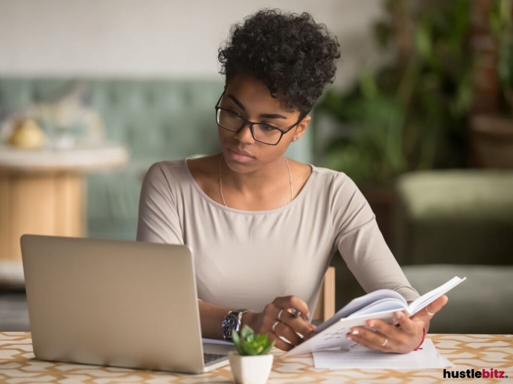 A focused woman working on a laptop while reviewing documents.