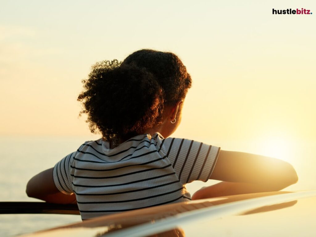 A woman outside of a car gazing looking to the sunset.