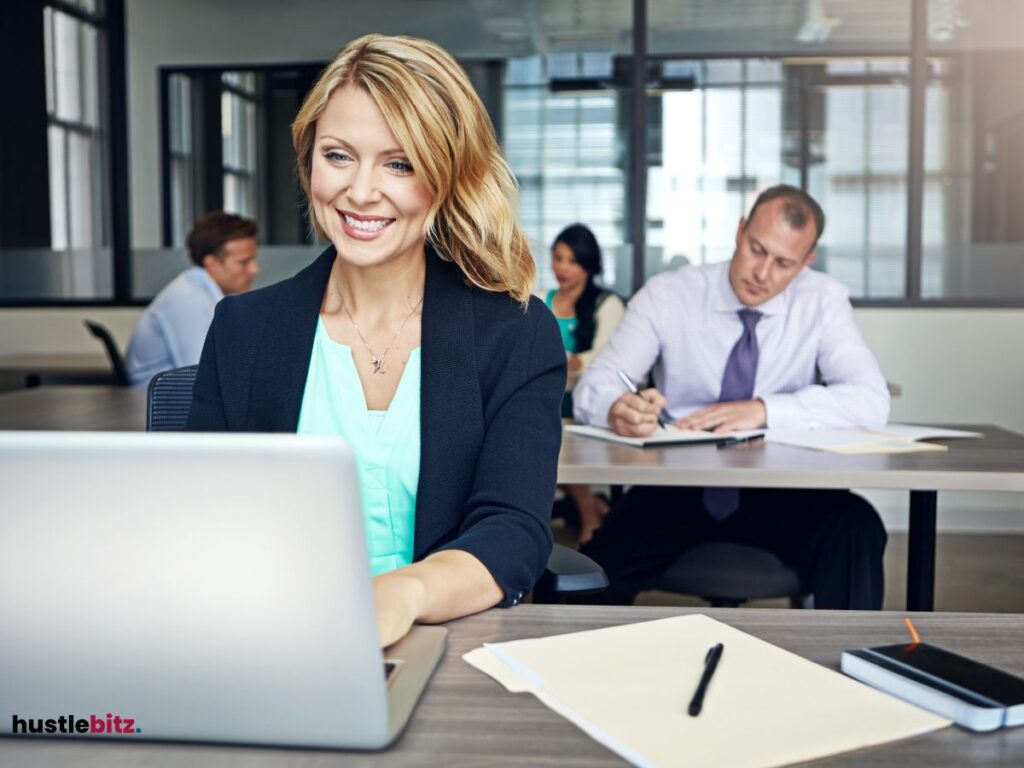A woman smiles looking at the laptop and a group of people background