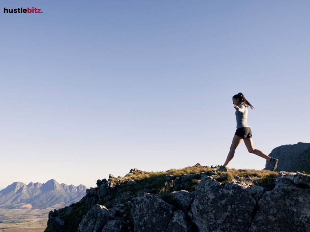 A woman confidently walking on rocky terrain, with mountains in the background.