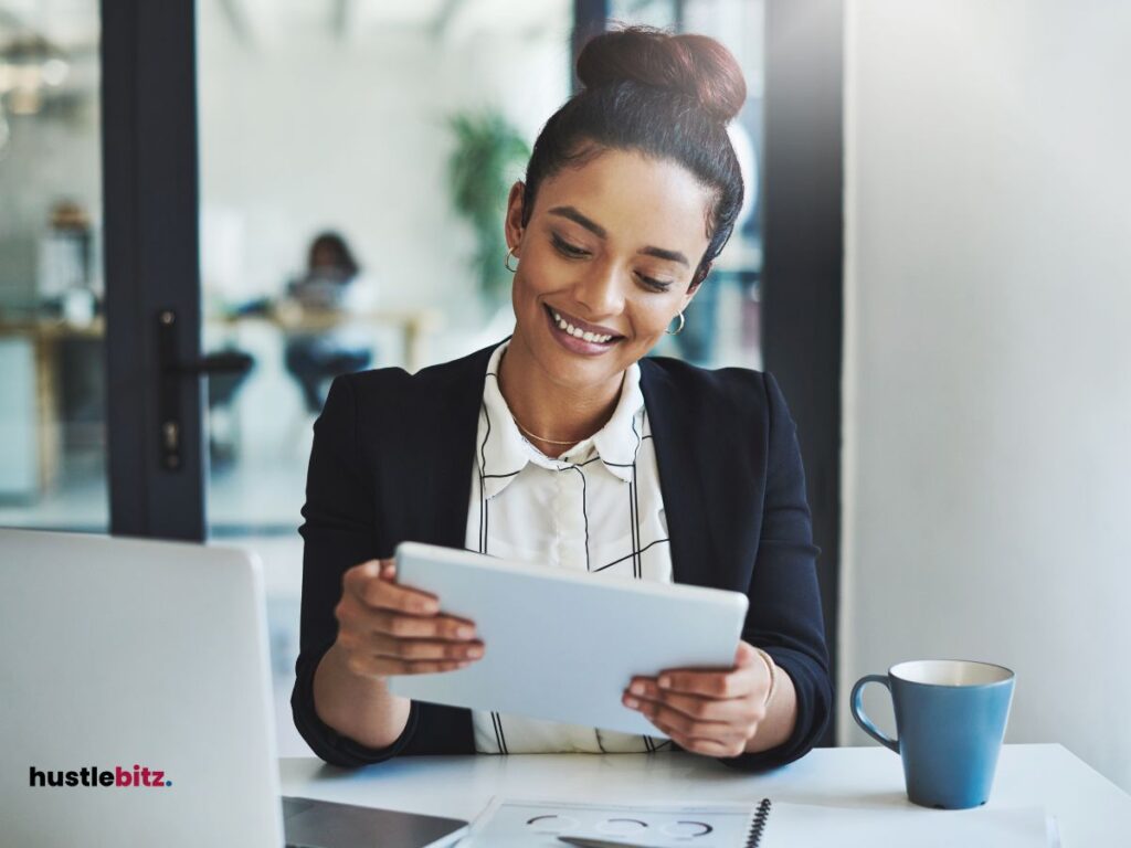 A smiling woman working on a tablet in an office.