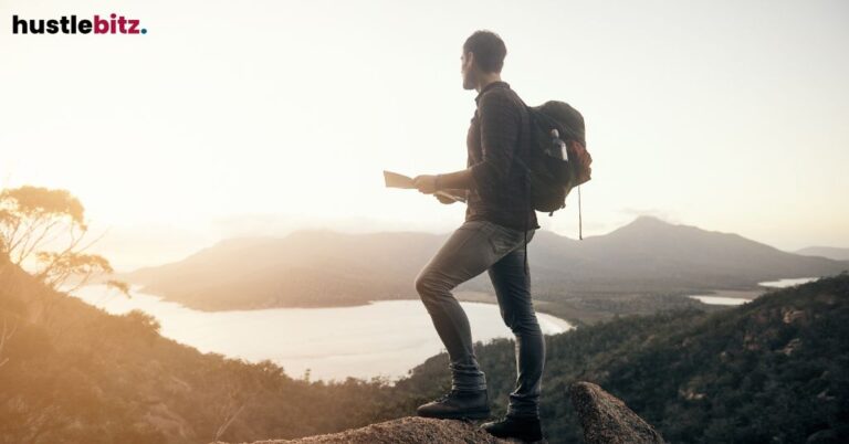 A man with a backpack standing on a cliff, holding a map, overlooking a vast landscape.
